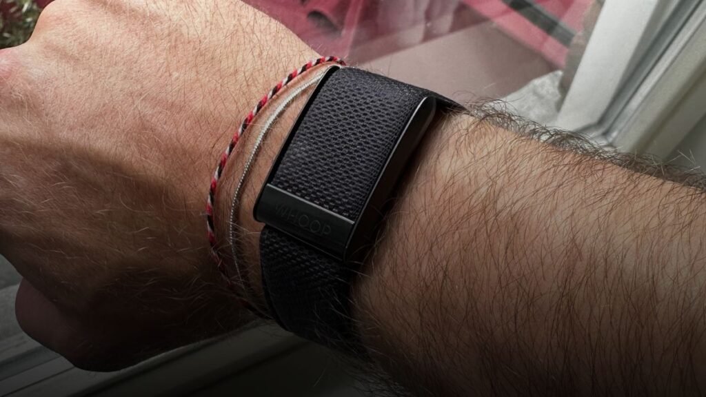 WHOOP wearable bandje op sportieve pols met herstel- en slaapstatistieken in de achtergrond