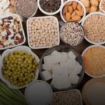 Verschillende plantaardige eiwitbronnen zoals linzen, tofu en noten op houten plank