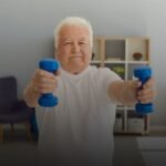 Oudere man doet krachttraining met dumbbells in een huis ter ondersteuning van spiermassa op latere leeftijd